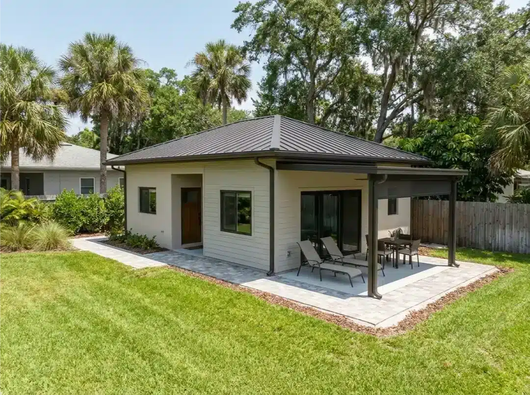Modern home addition with white siding and metal roof, featuring a covered patio with outdoor furniture.