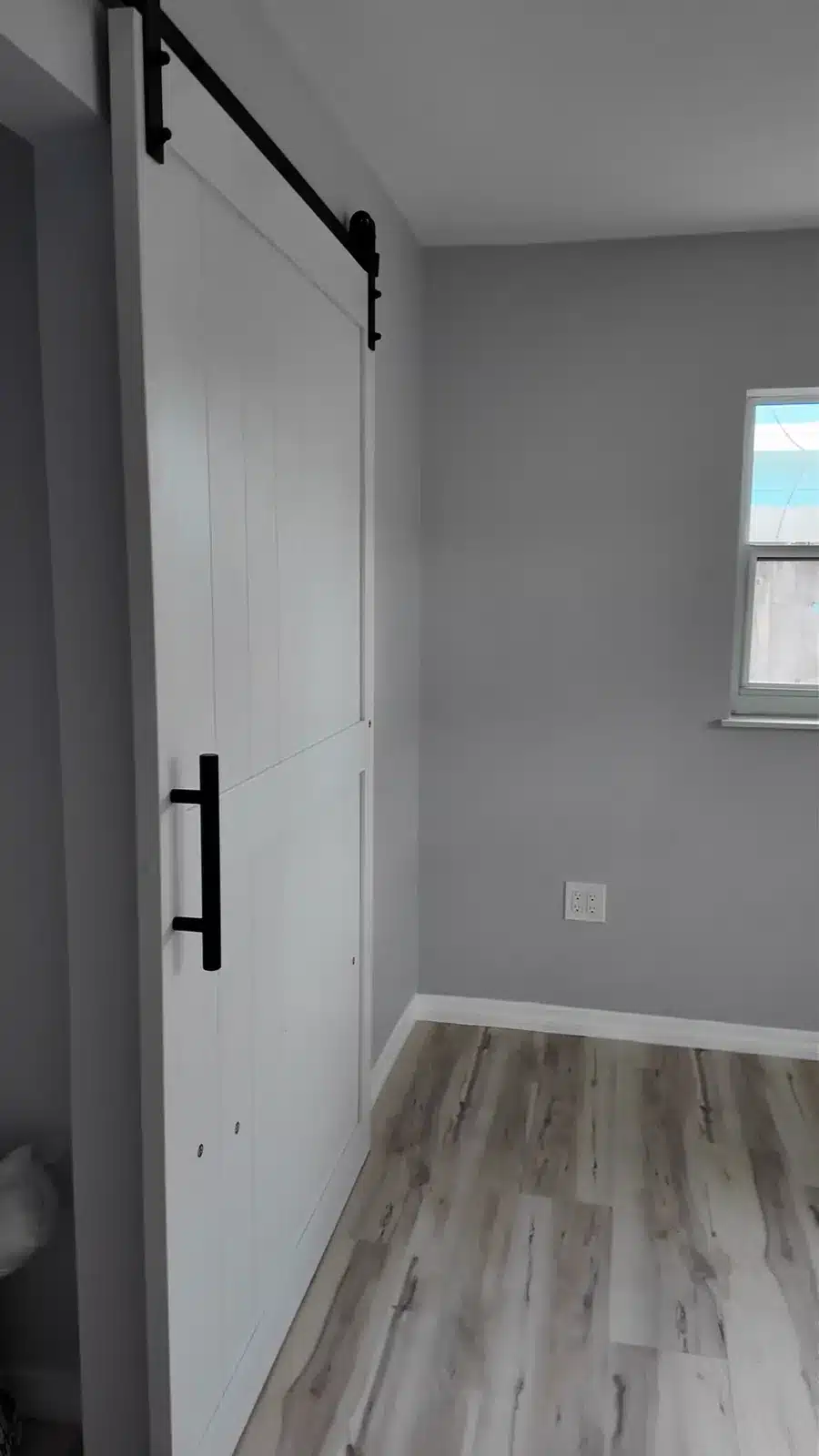 White sliding barn door on black track opening into a renovated grey bedroom