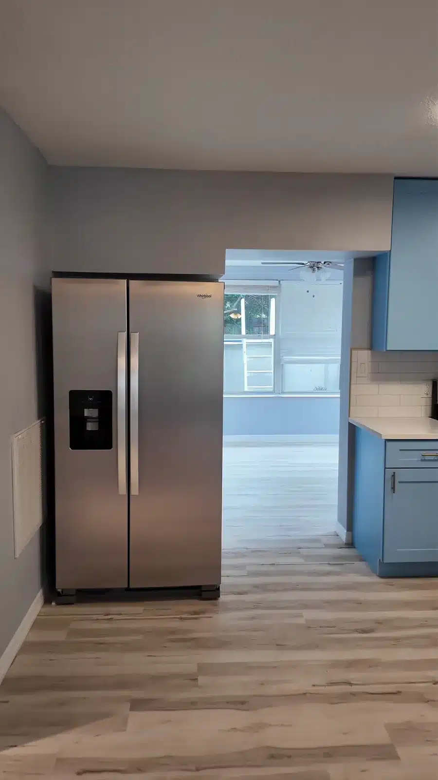 Living area with new plank flooring looking through to the kitchen and stainless refrigerator