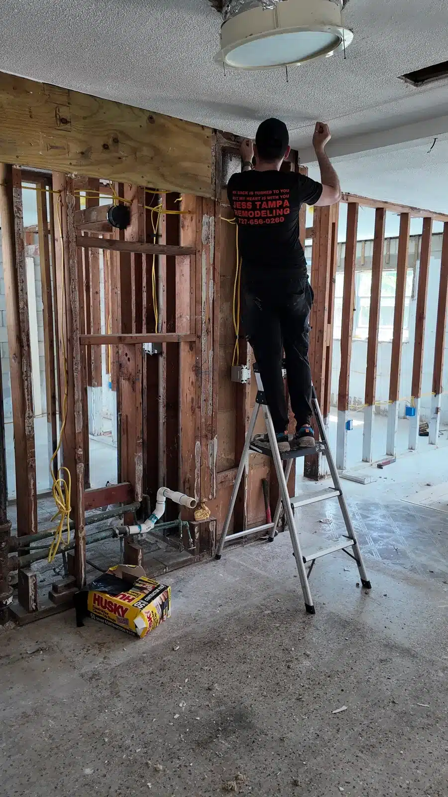 Crew member on a ladder working on the opened stud wall between the kitchen and living area